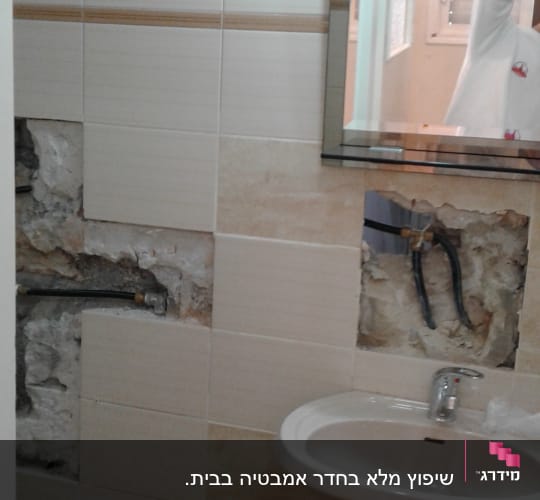 קיר אמבטיה עם אריחים שבורים וצנרת חשופה